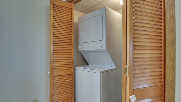 Un lavadero pequeño con lavadora y secadora integradas, puertas de madera con listones y un enchufe eléctrico a la vista.