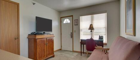 A living room with a television on a wooden cabinet, a couch, a door, and a window with blinds.