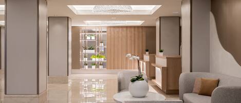 A modern lobby with a central seating area, a wooden panel wall with plants, and a skylight.