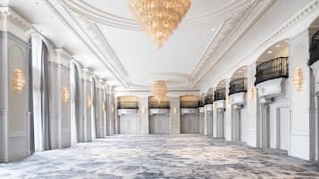 A grand hallway with a patterned carpet, ornate columns, and a large chandelier.