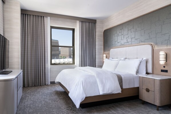 A modern hotel room with a large bed, a desk, and a view of the cityscape through a window. - The Westin Book Cadillac Detroit (Detroit)
