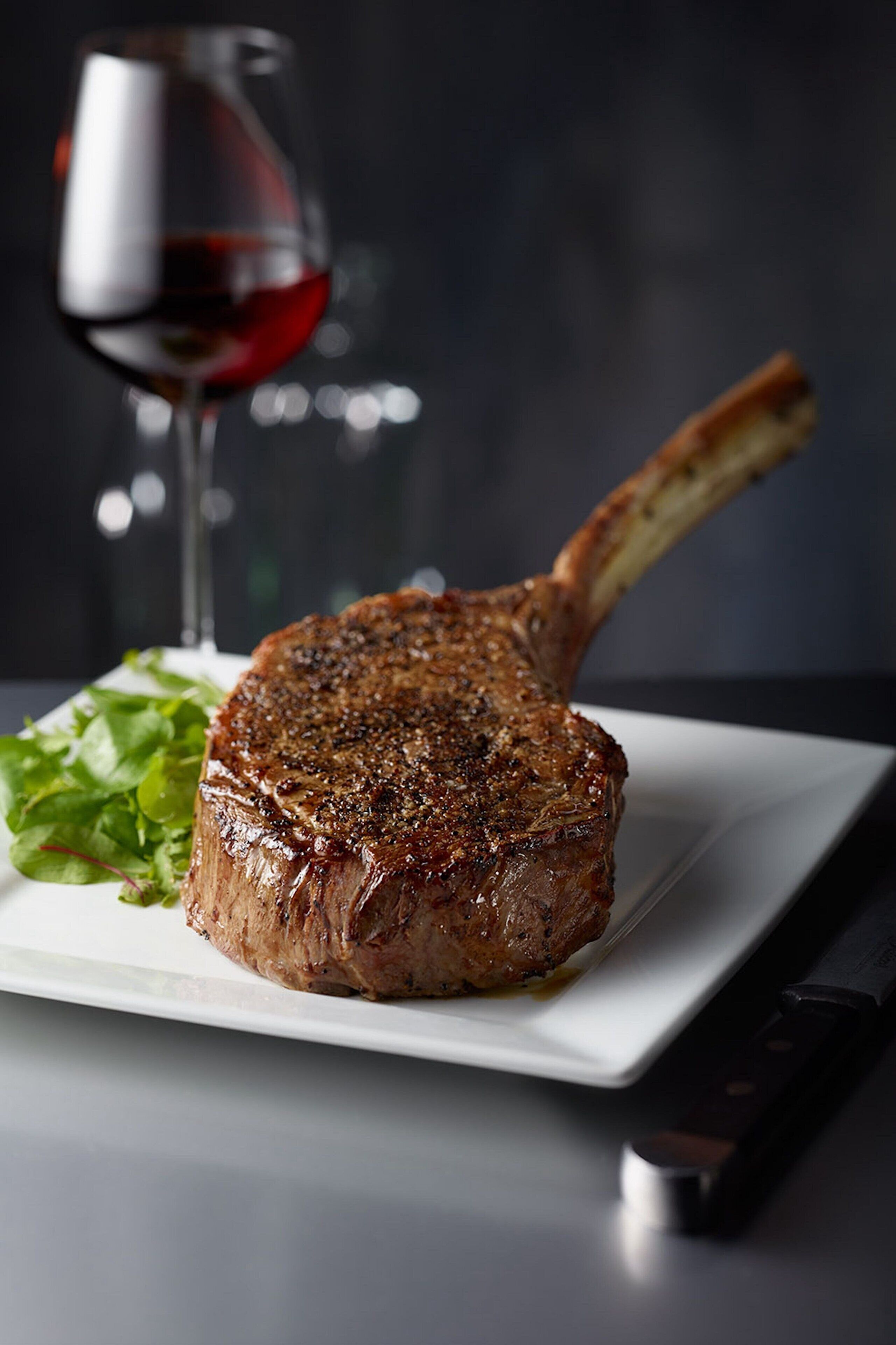 A steak with a side of greens and a glass of red wine on a white plate.