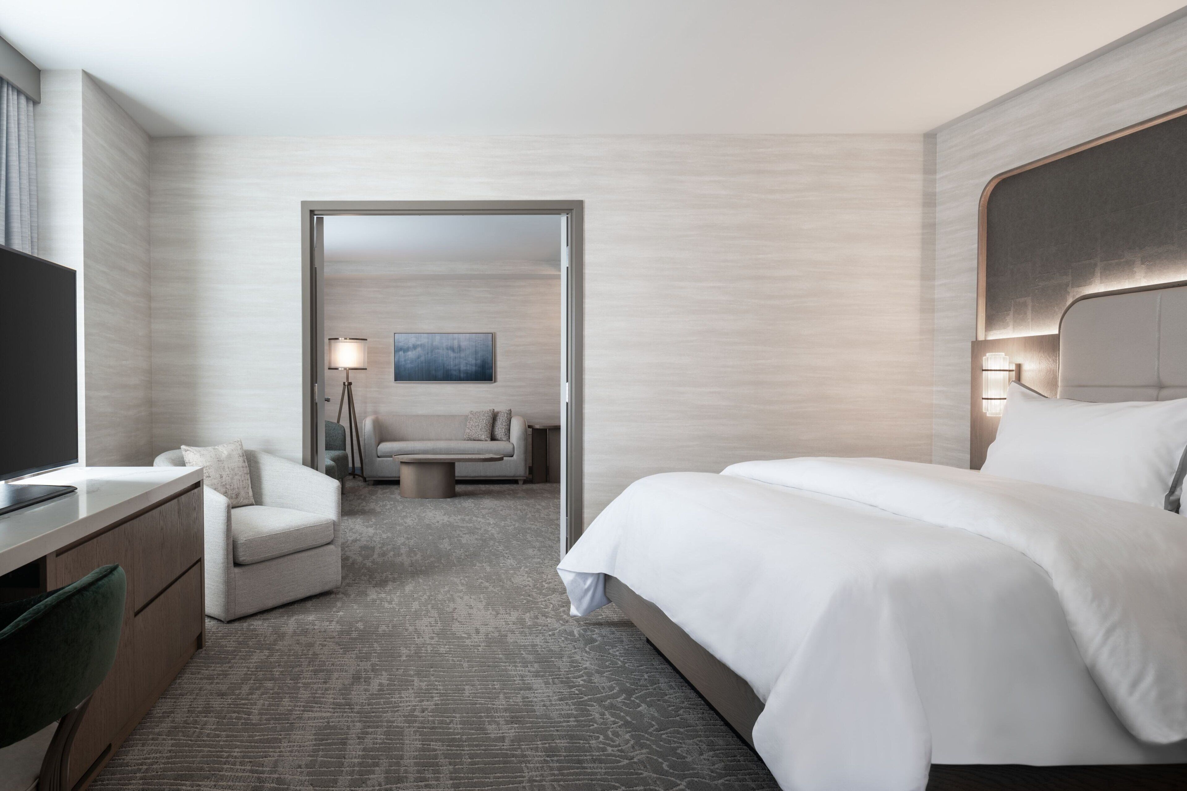 Een hotelkamer met een bed, een bureau, een stoel, een lamp en een schilderij aan de muur.