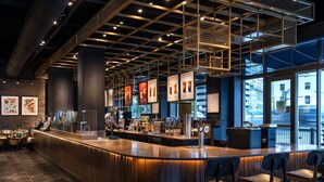 A modern bar area with a curved counter, bar stools, and a view of the city through large windows. - The Westin Book Cadillac Detroit (Detroit)