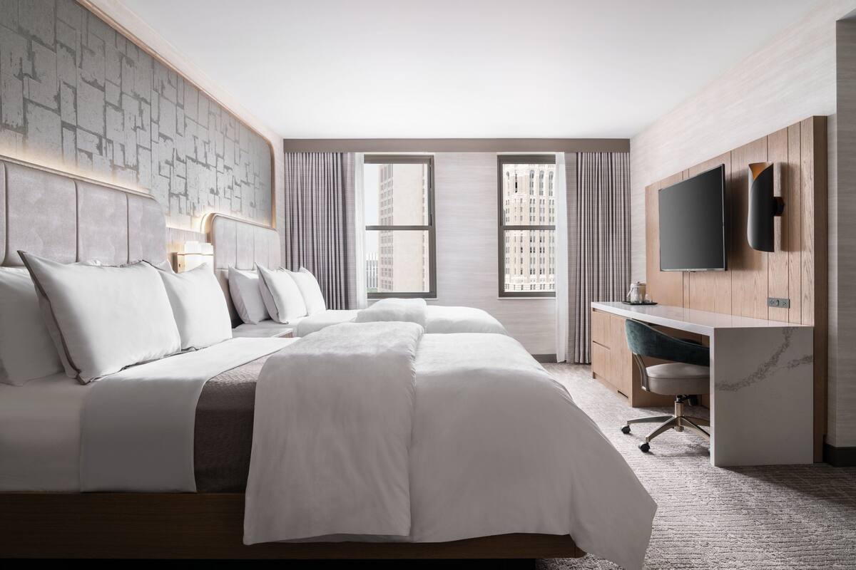 A modern hotel room with a large bed, a desk, a TV, and a city view.