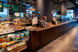 Un interior moderno de cafetería con mostrador, vitrinas de pasteles y una pizarra con el menú.
