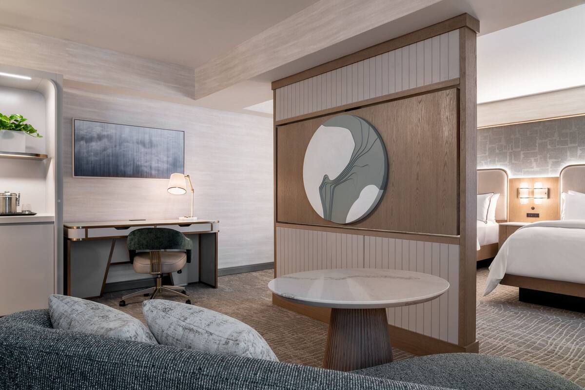 A modern hotel room with a desk, a round table, a bed, and a large abstract artwork on the wall.