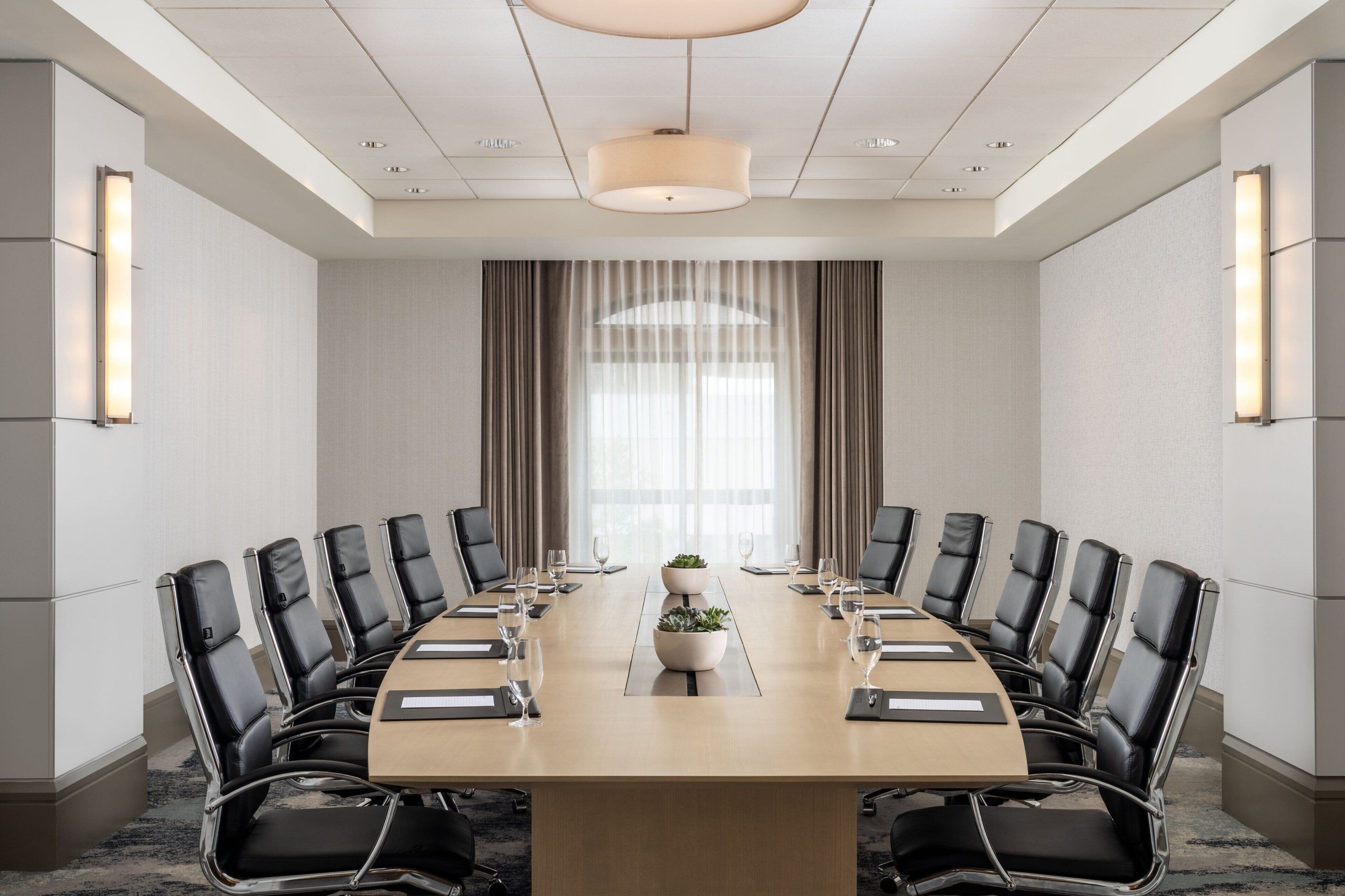 A conference room with a long table, black leather chairs, and a central plant.