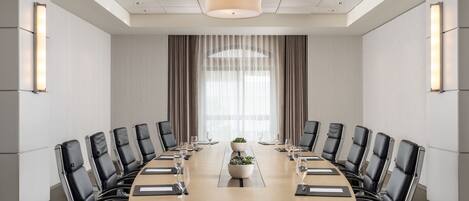 A conference room with a long table, black leather chairs, and a central plant.