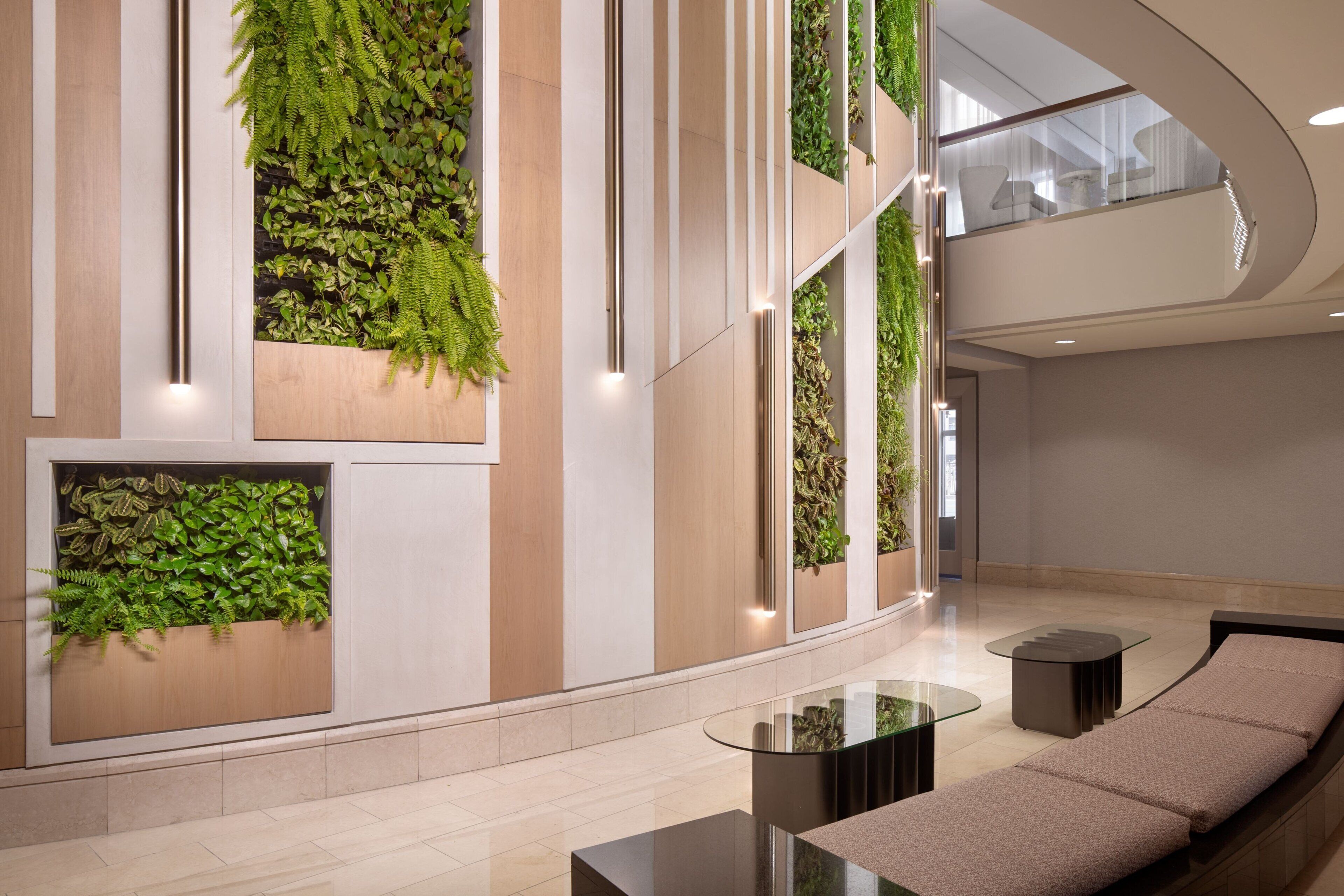 Un hall d’entrée moderne agrémenté de jardins verticaux, d’un canapé aux lignes courbes et d’une table basse en verre.