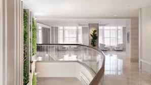 A modern hotel lobby with a glass railing, a seating area with white chairs, and a green vertical garden. - The Westin Book Cadillac Detroit (Detroit)
