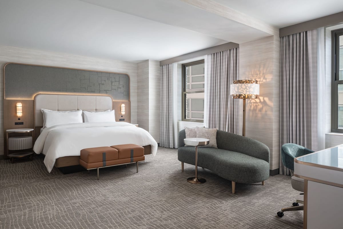 A modern hotel room with a large bed, a small sofa, a desk, and a lamp.