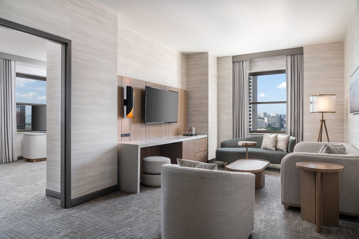 A modern hotel room with a flat-screen TV mounted on a wooden panel, a sofa, a small coffee table, and a lamp.
