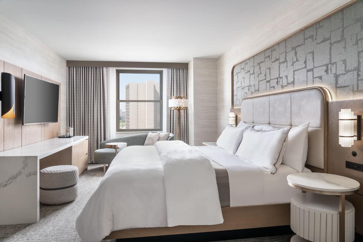 A modern hotel room with a large bed, a desk, a chair, and a TV.