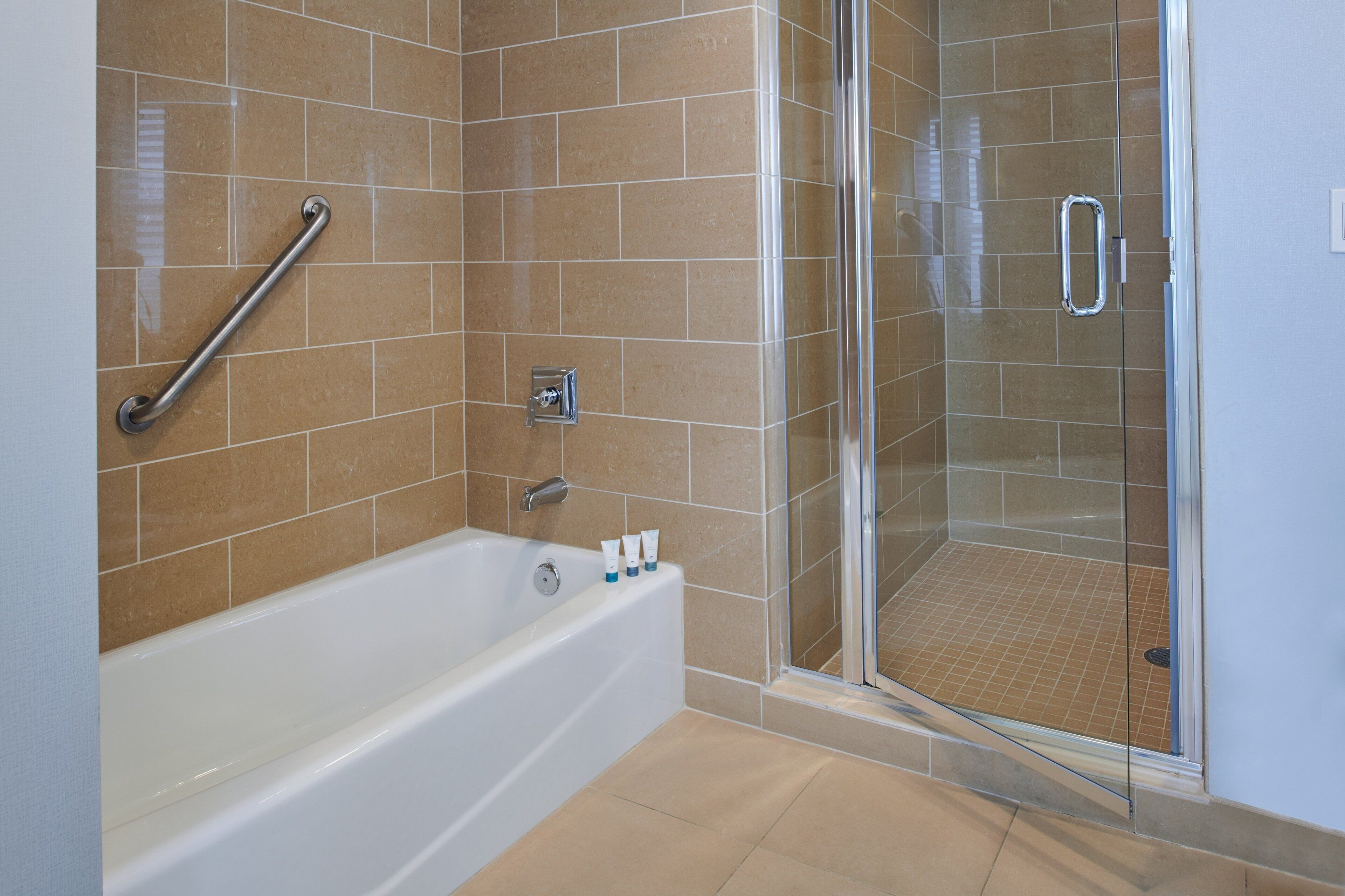 A bathroom with a bathtub, a glass shower enclosure, and a handrail.