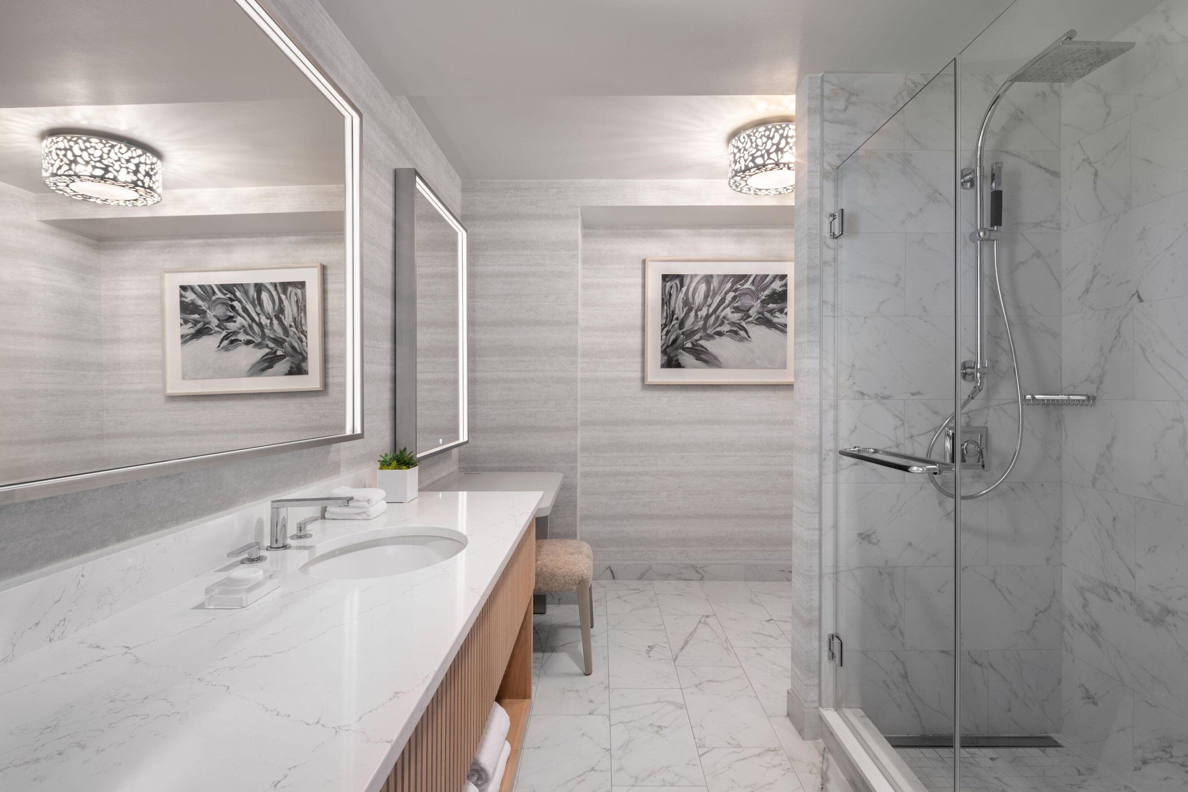 A modern bathroom with a large mirror, two sinks, a shower, and artwork on the walls.