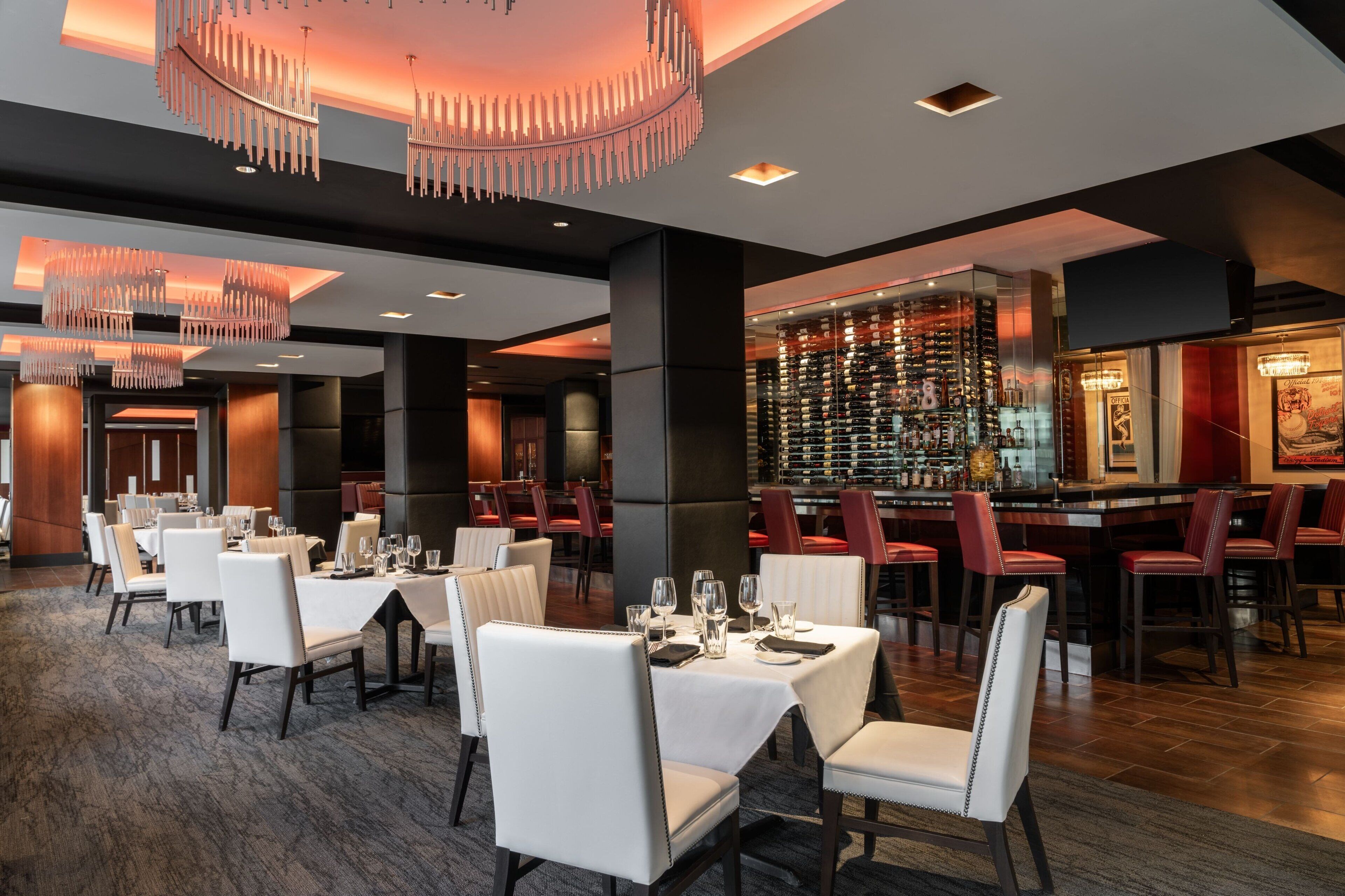Een modern restaurant met witte tafels en stoelen, een bar en een wijnrek.