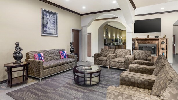 A spacious living room with patterned sofas, a coffee table, and a flat-screen TV mounted on the wall. - Best Western Red River Inn & Suites (Thackerville)