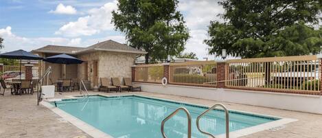 A swimming pool with a stone deck, lounge chairs, and umbrellas.