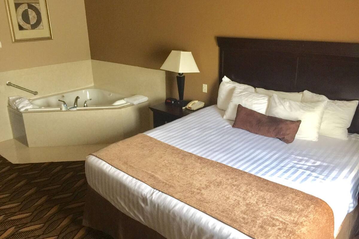 Una habitación de hotel con una cama grande, una bañera independiente, una lámpara de noche y un teléfono en la mesita.
