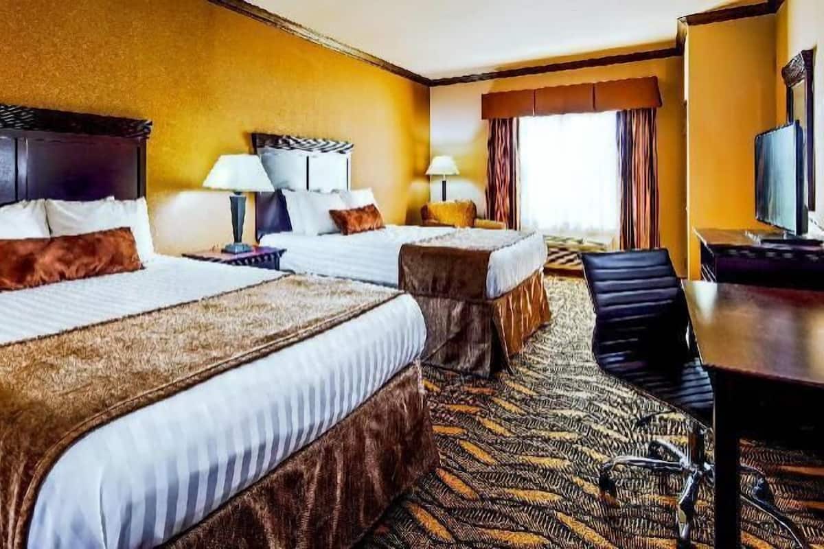 Habitación de hotel con dos camas, un escritorio, una silla, lámparas y televisión.