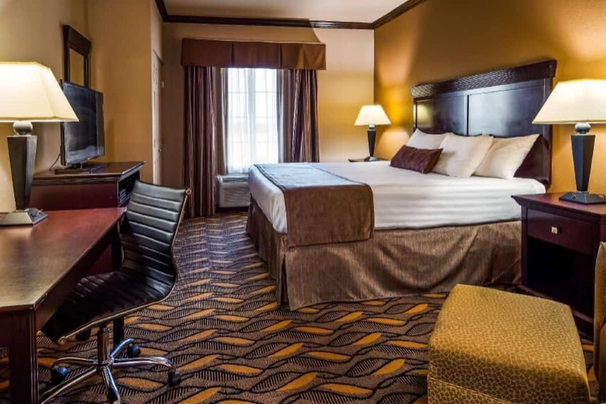 Habitación de hotel con cama, dos mesitas de noche, escritorio, silla, televisor y ventana con cortinas.