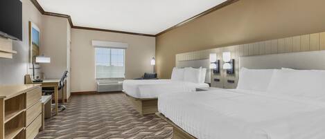 A hotel room with two beds, a desk, a TV, and a window.