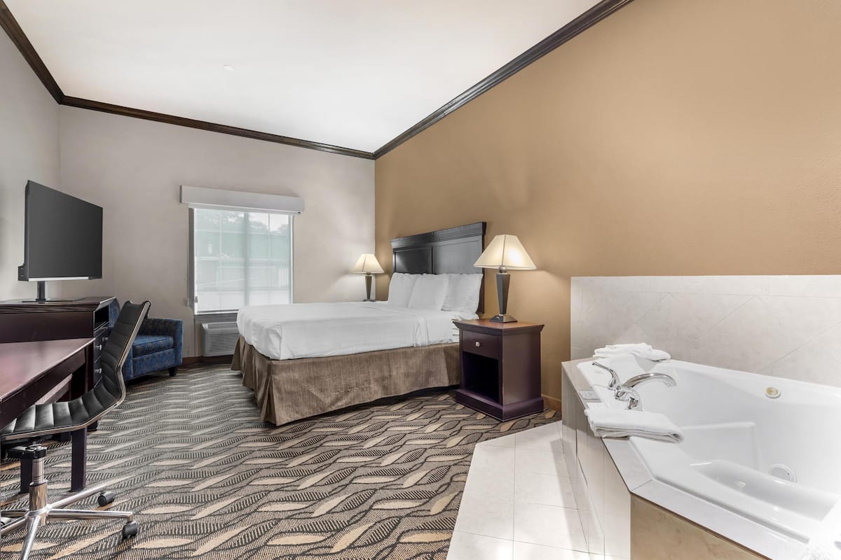 Habitación de hotel con cama, dos lámparas de noche, un escritorio con silla, un ventanal grande y una bañera.