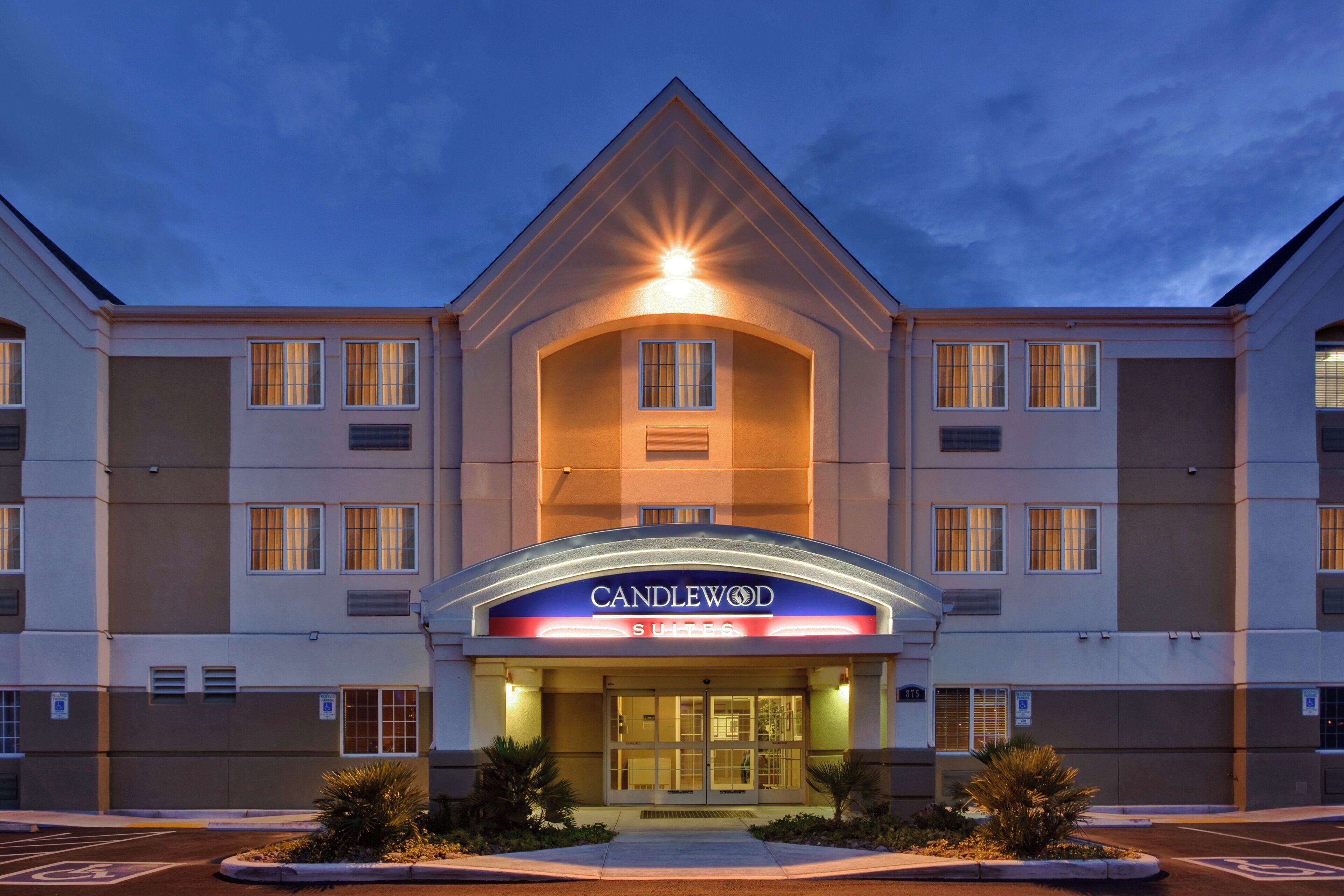 Un hotel con una entrada destacada, un cartel que dice 'CANDLEWOOD SUITES' y un estacionamiento con espacios reservados para discapacitados.