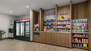 Una tienda con sección refrigerada, microondas y estantes llenos de aperitivos y bebidas.
