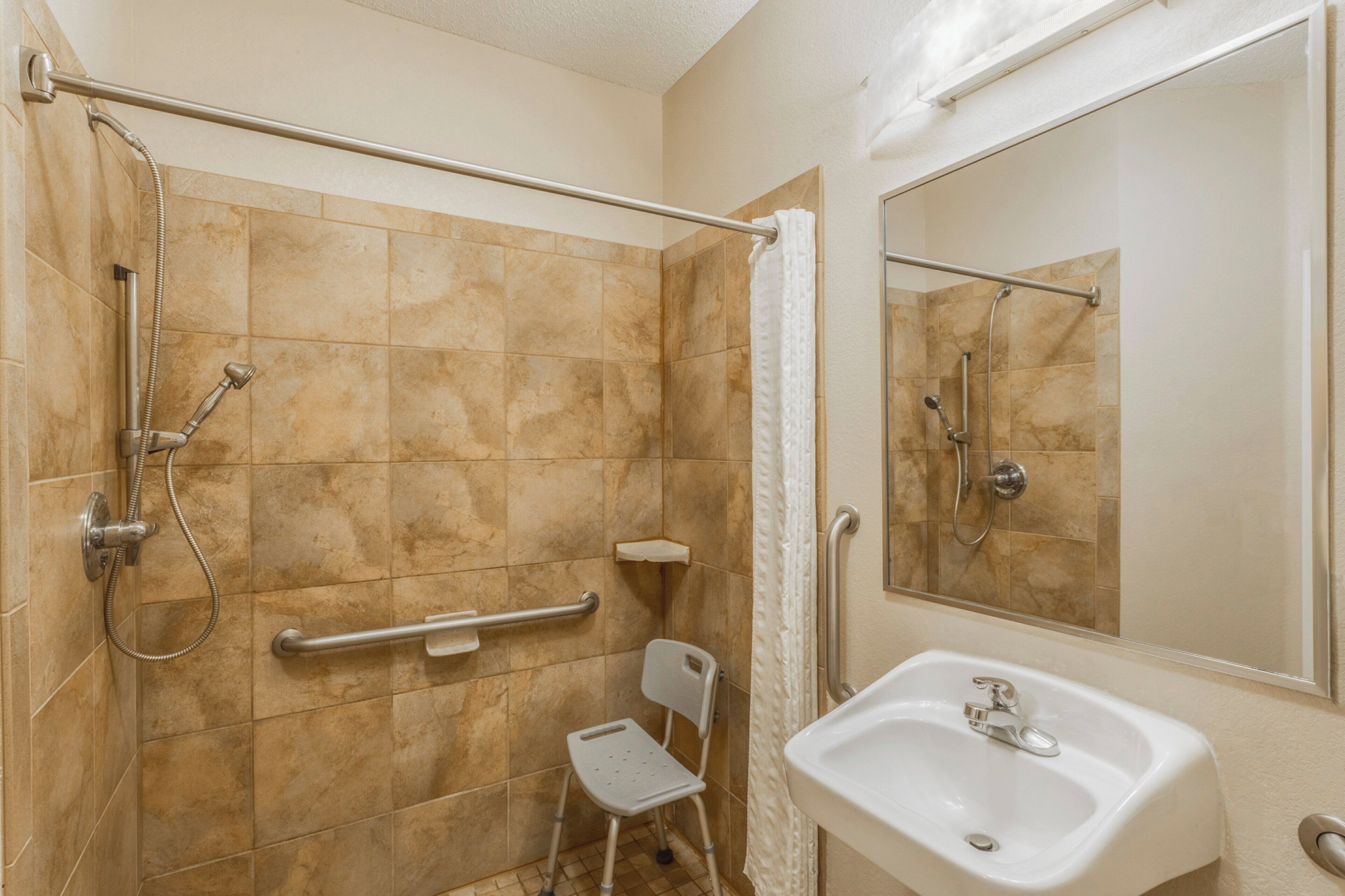 Une salle de bain équipée d’une douche, d’une barre d’appui, d’une petite chaise et d’un lavabo.
