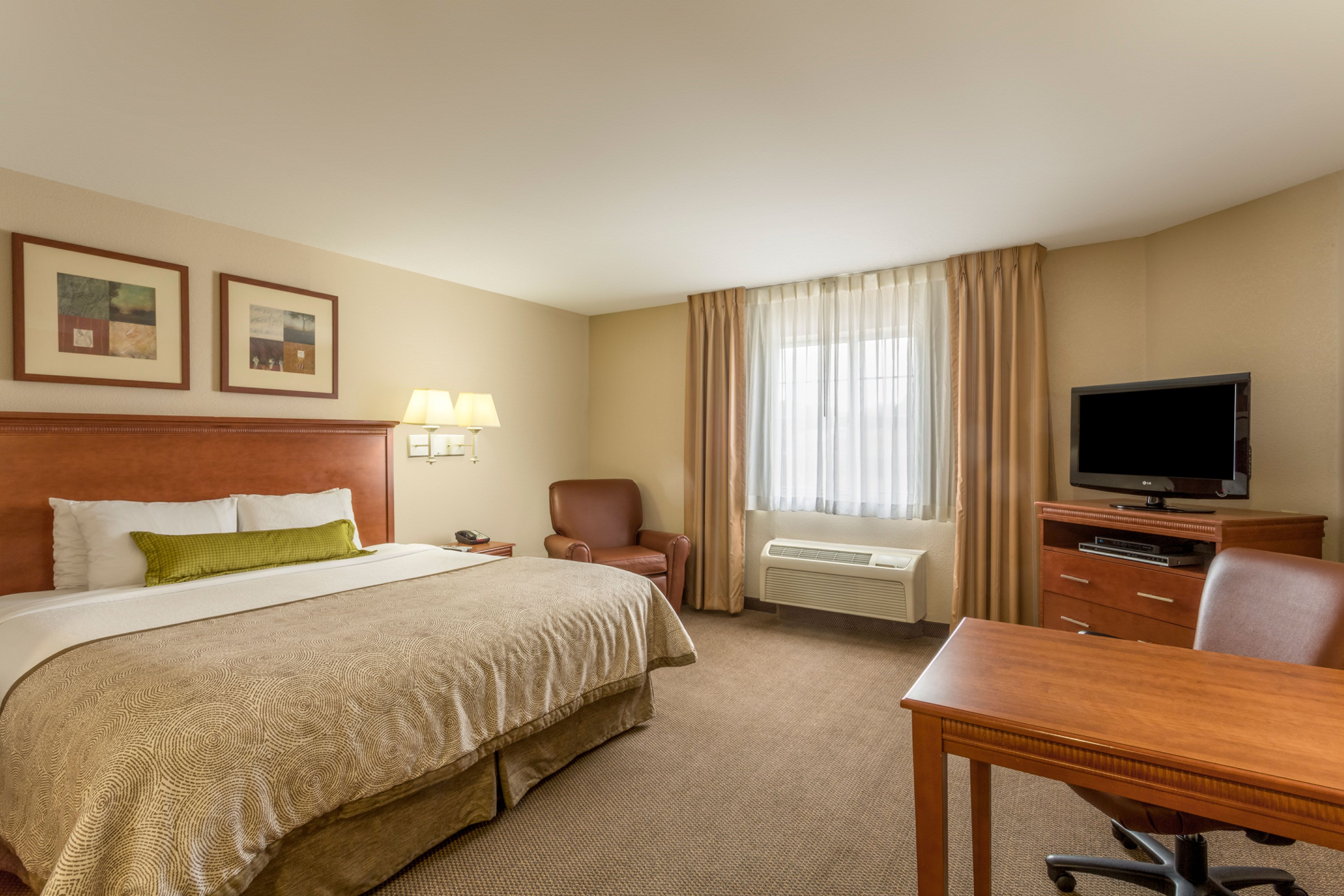 A hotel room with a large bed, a desk, a chair, a television, and a window with curtains.