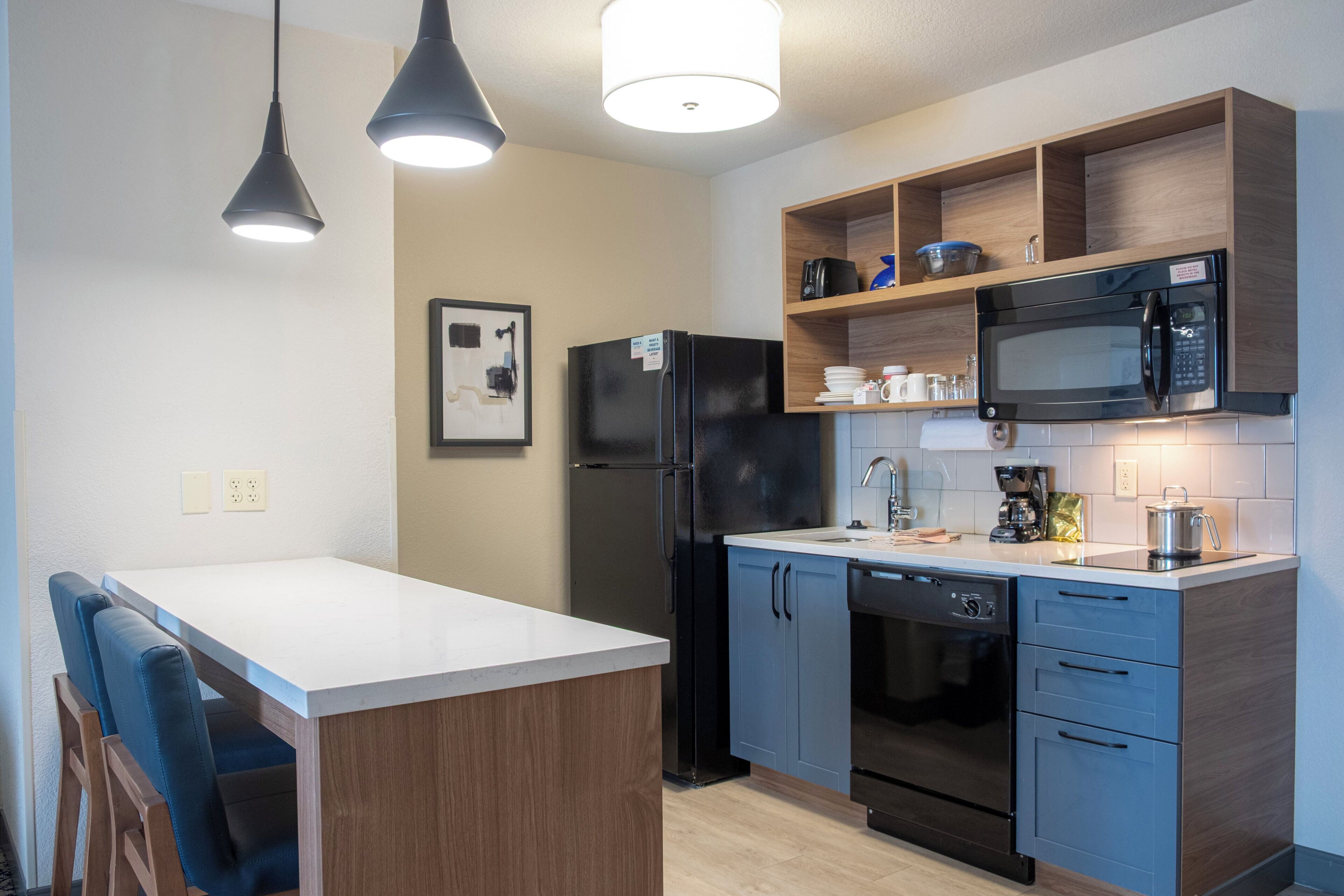 A modern kitchen with a central island, black appliances, and wooden shelving.