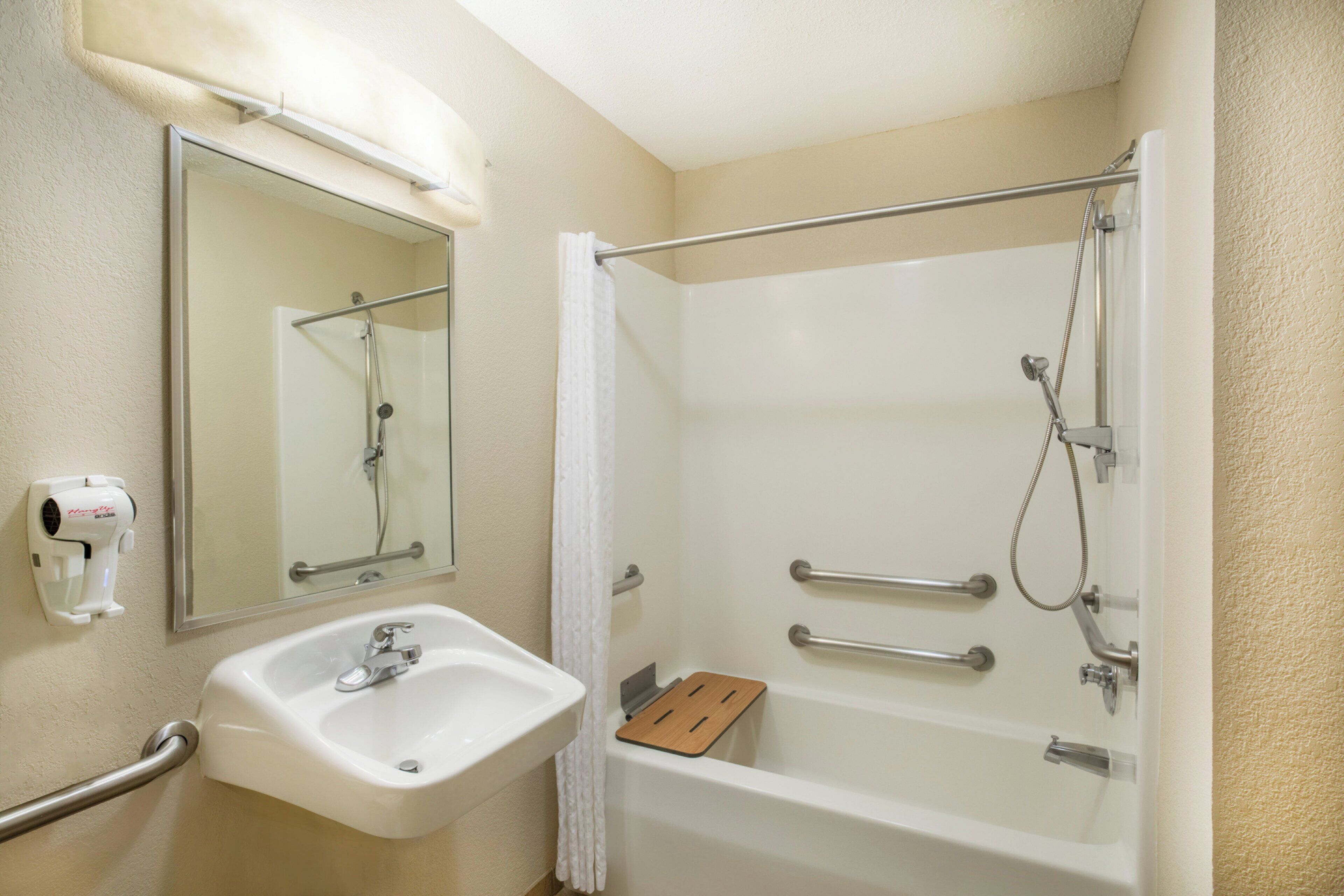 Un baño con lavamanos blanco, un espejo, ducha con cabezal de ducha manual y secador de mano.