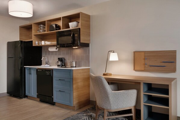 Una cocina moderna con microondas integrado, refrigerador y lavavajillas. Hay un escritorio de madera con una silla y una lámpara.