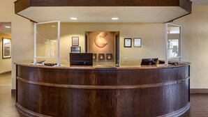 Un mostrador de recepción con detalles de madera, un logotipo grande iluminado en la pared y certificados enmarcados en la pared de fondo.