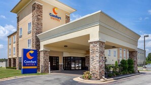Un hotel Comfort Suites con fachada de piedra, entrada cubierta y cielo despejado.