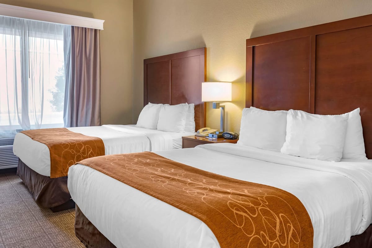 A hotel room with two beds, a nightstand with a lamp, and a window with curtains.