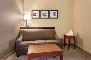 Une chambre d’hôtel avec un canapé, une petite table, une lampe et trois tableaux encadrés accrochés au mur.