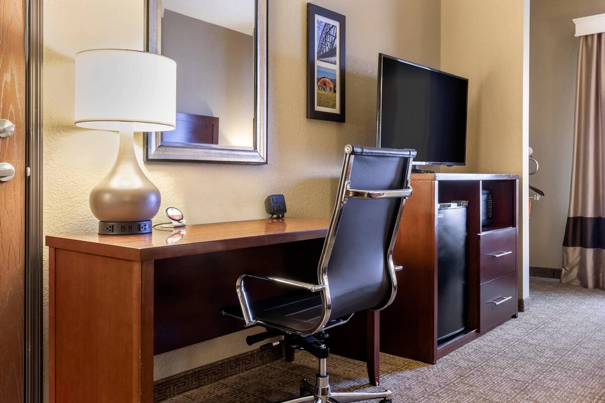 A hotel room with a desk, a chair, a television, a mirror, and a dresser.