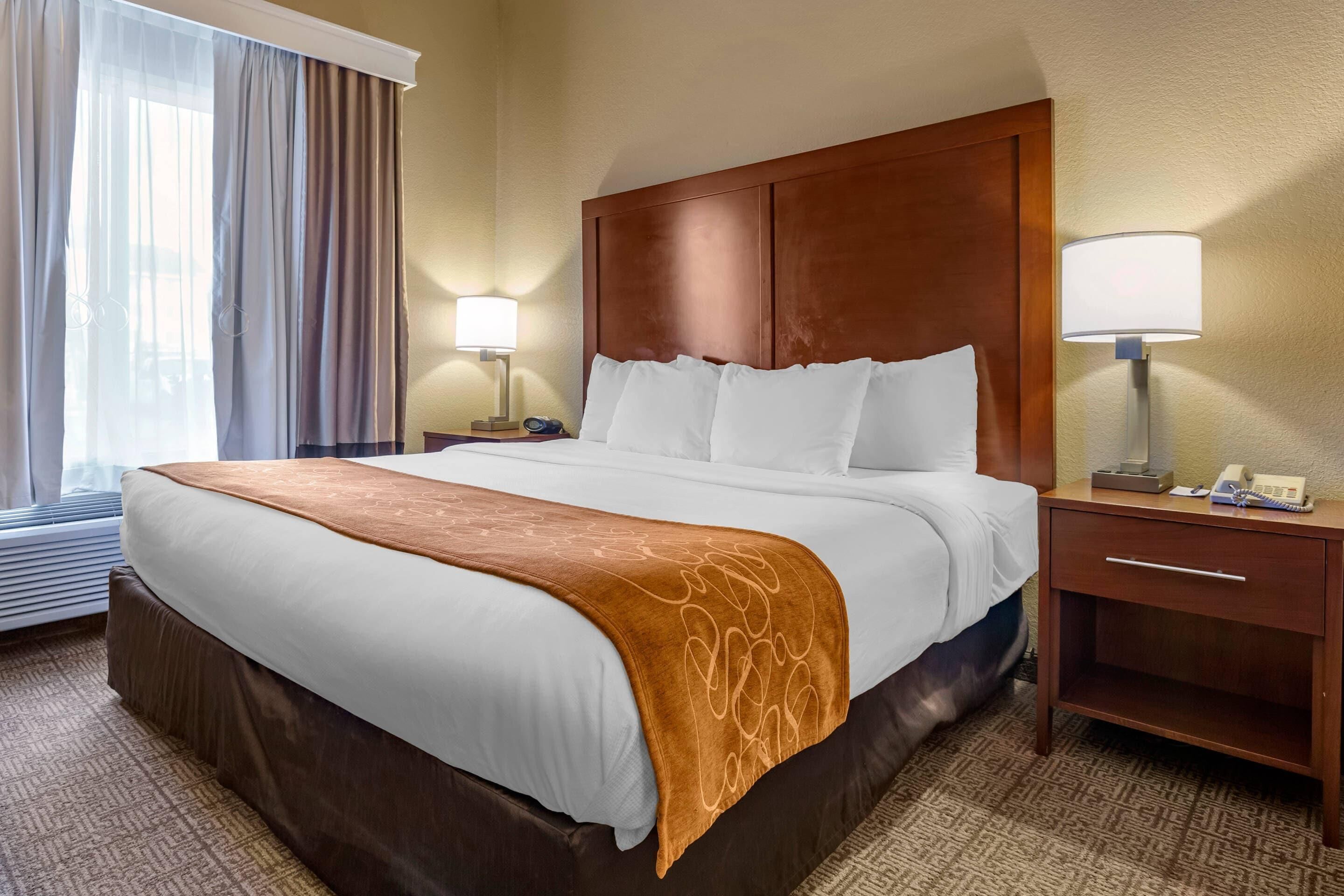 A hotel room with a large bed, two bedside tables, a nightstand, a lamp, and a window with curtains.
