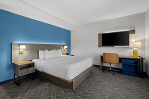 Habitación de hotel con cama, mesitas de noche, escritorio con silla, televisor de pantalla plana y lámpara.