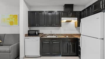 A compact kitchen with dark cabinets, a white refrigerator, a microwave, and a dishwasher.