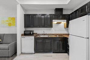 Una cocina compacta con armarios oscuros, un refrigerador blanco, un microondas y un lavavajillas.