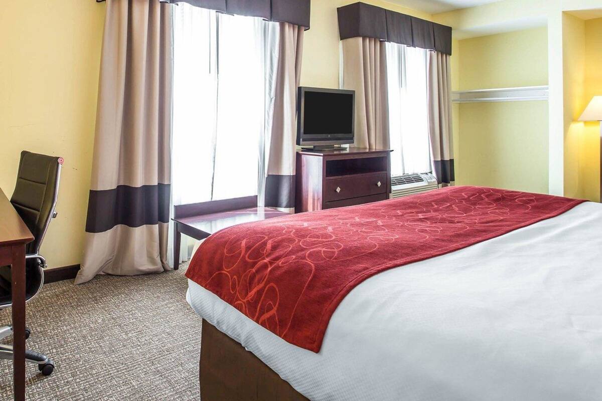 Une chambre d’hôtel avec un lit, un bureau, une télévision et des rideaux.