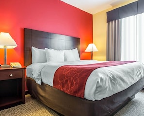 A hotel room with a large bed, two bedside lamps, a nightstand, and a window with curtains.