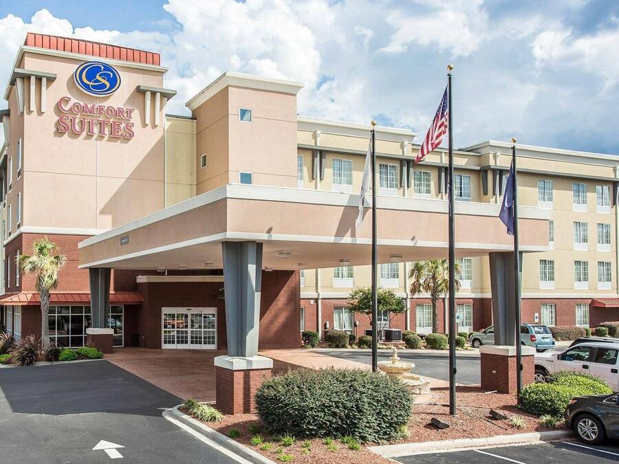 A hotel with a prominent Comfort Suites sign, a covered entrance, and a flagpole with the American flag.
