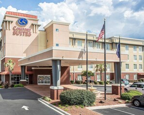 Un hotel con un llamativo letrero de Comfort Suites, una entrada cubierta y un asta con la bandera estadounidense.