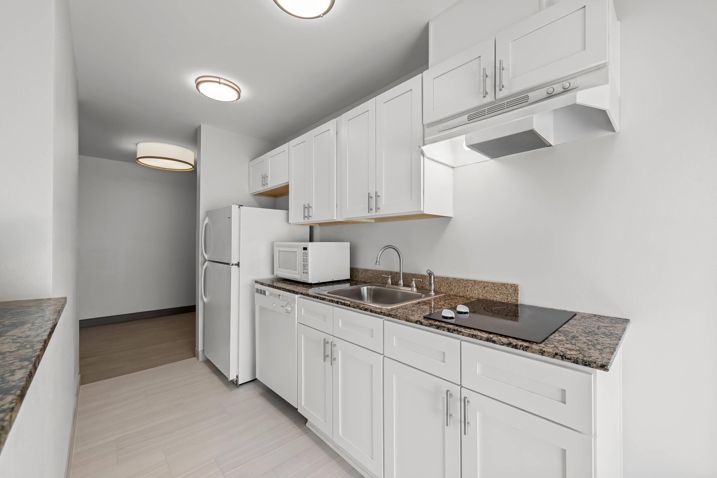 A modern kitchen with white cabinetry, a built-in microwave, a stainless steel sink, and a granite countertop.