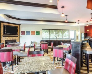 Een restaurant met meerdere tafels en stoelen, een flatscreen televisie aan de muur en een groot raam met uitzicht op het omliggende landschap.